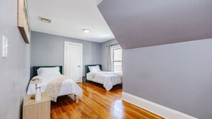 Een slaapkamer met twee bedden, een houten vloer, een witte deur en een raam.