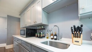 Een moderne keuken met witte kasten, een roestvrijstalen spoelbak, een magnetron en een messenblok.