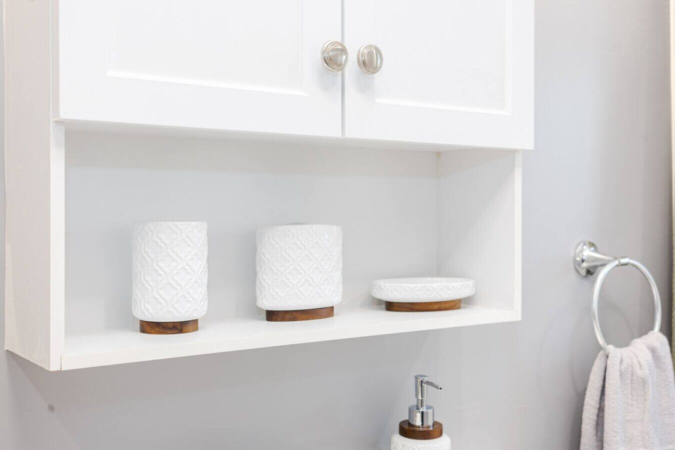 Un baño blanco con un mueble blanco sobre una repisa que sostiene dos toallas blancas y un dispensador de jabón blanco.
