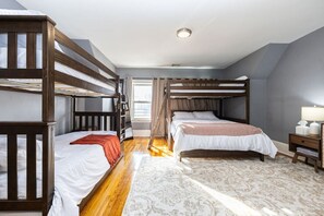 A dormitory room with bunk beds, a window with curtains, a bedside table with a lamp, and a patterned rug. - Cozy 3BD/1BA in Boston | Franklin Zoo, Boston Comm (Boston)