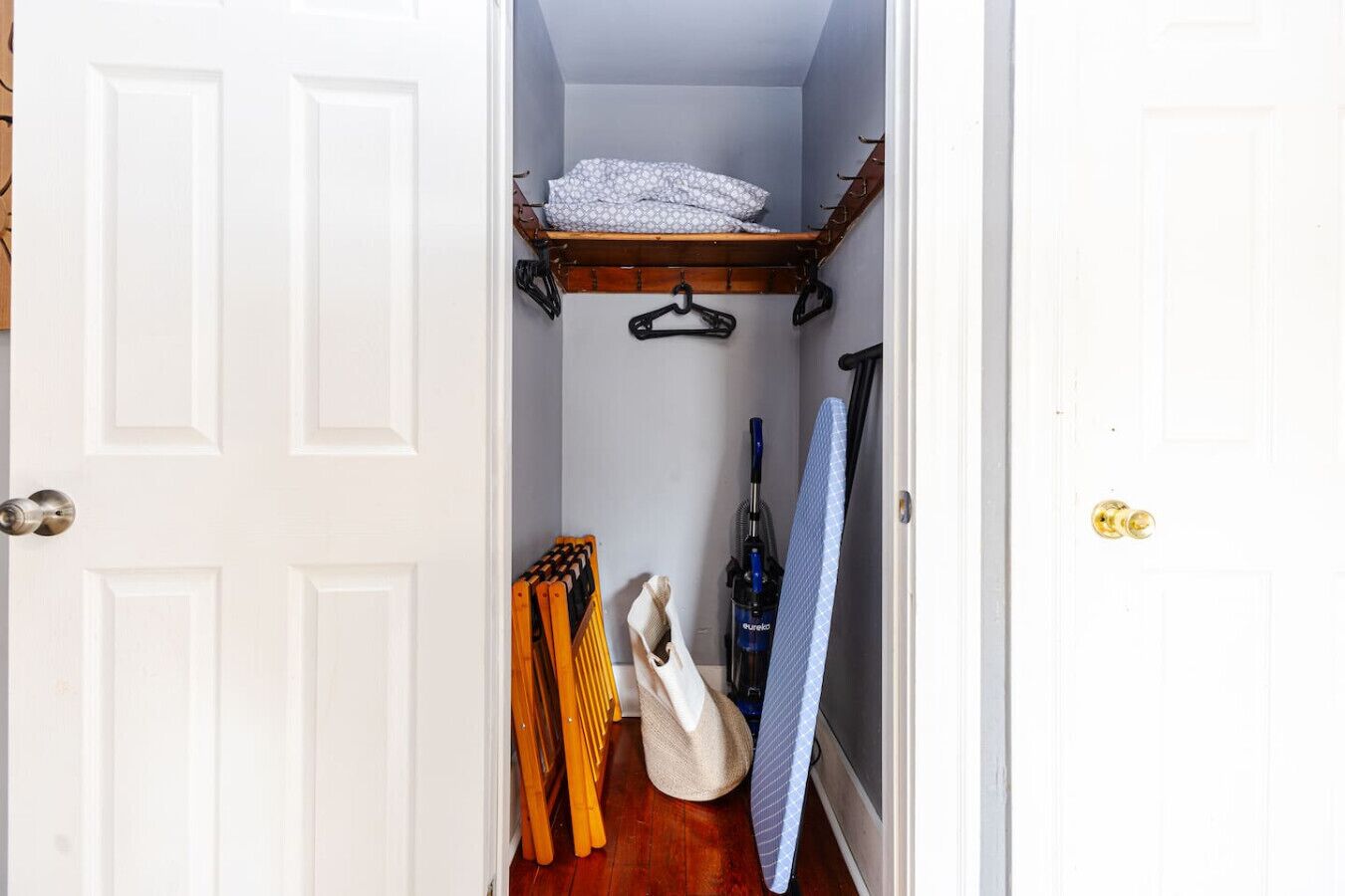 A narrow hallway with a wooden shelf above a door, a vacuum cleaner, and a suitcase on the floor.