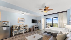 Une chambre d’hôtel comprenant un lit, un bureau avec des chaises, une télévision, un ventilateur de plafond et un balcon avec vue.