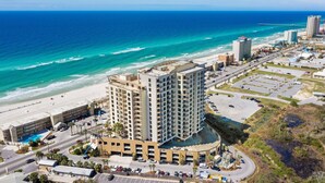 Un grand hôtel avec de nombreuses étages, offrant une vue sur la plage, doté de parkings et avec une jetée en arrière-plan.