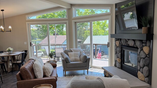 A spacious living room with a fireplace, large windows, and a dining area. - Beach House w/ Huge Deck Amazing Views!! Kayaks, Swim, Fish! Golf Cart Rental! (Salem Lakes)