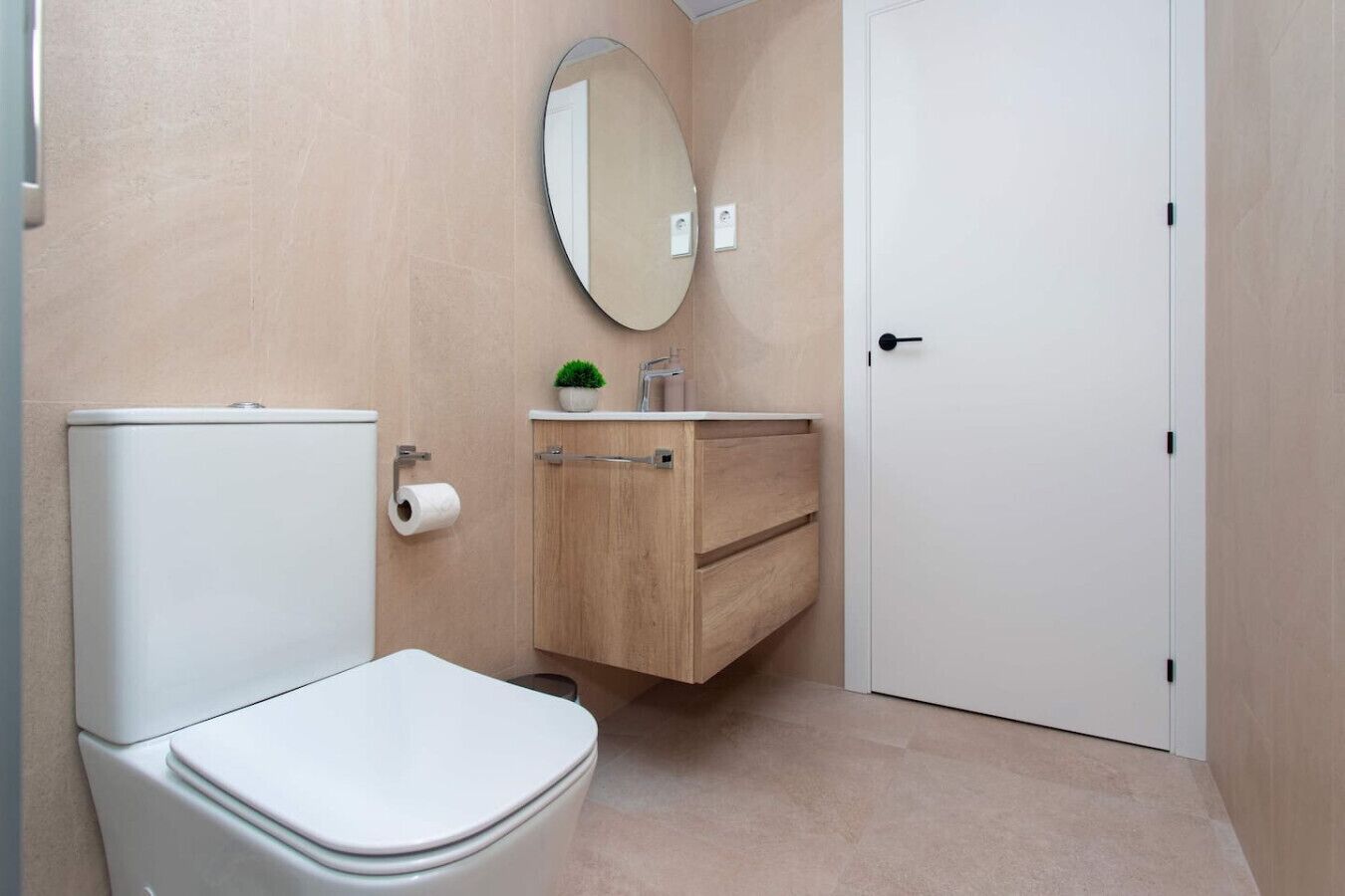 A small, clean bathroom with a toilet, a wooden cabinet with a mirror, and a door.