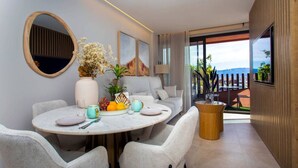 A modern dining area with a round table, grey upholstered chairs, a vase with flowers, and a fruit bowl. - Luxury UCAM Studio | Desk & High-Speed Wi-Fi (Guadalupe)