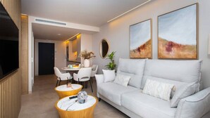 A modern living room with a white sofa, two wooden coffee tables, and a dining area with white chairs. - Luxury UCAM Studio | Desk & High-Speed Wi-Fi (Guadalupe)