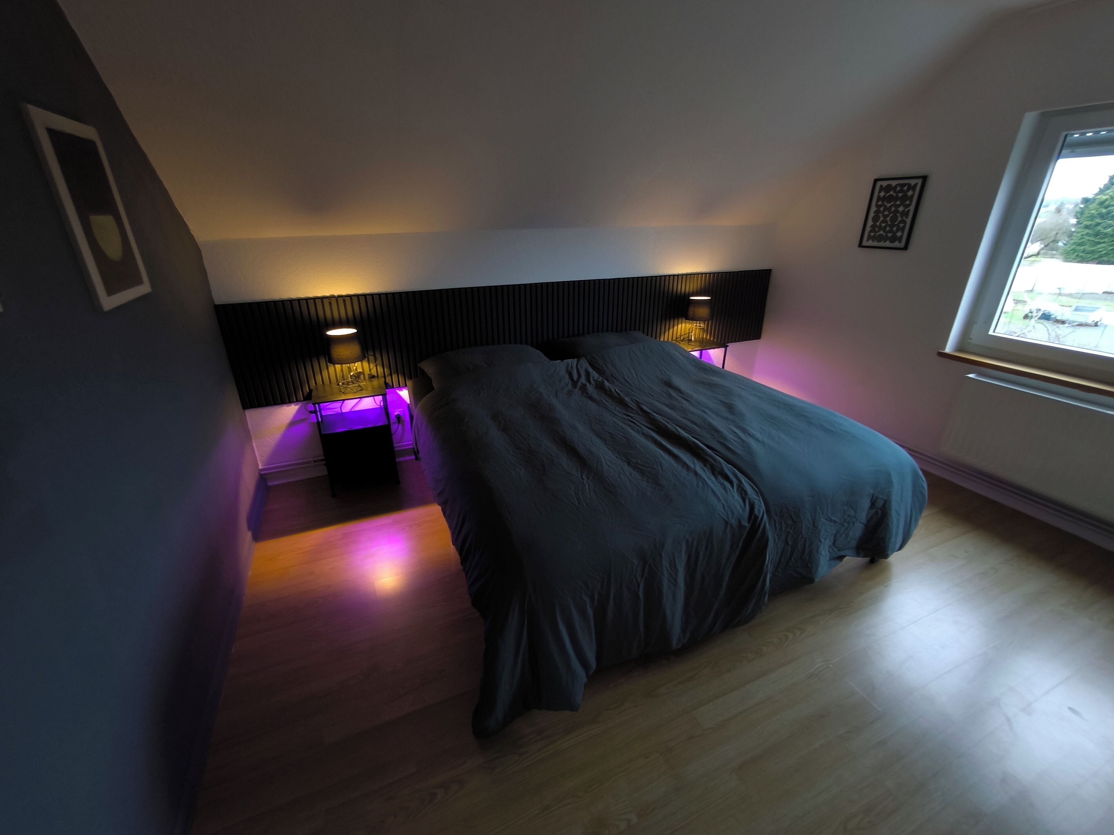 Een slaapkamer met een bed, twee bedlampjes, een raam en een vastgezet hoofdbord.