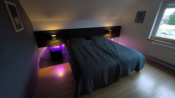 Een slaapkamer met een bed, twee bedlampjes, een raam en een vastgezet hoofdbord.