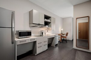 Cocina compacta equipada con microondas, cafetera y un pequeño comedor con mesa y silla.