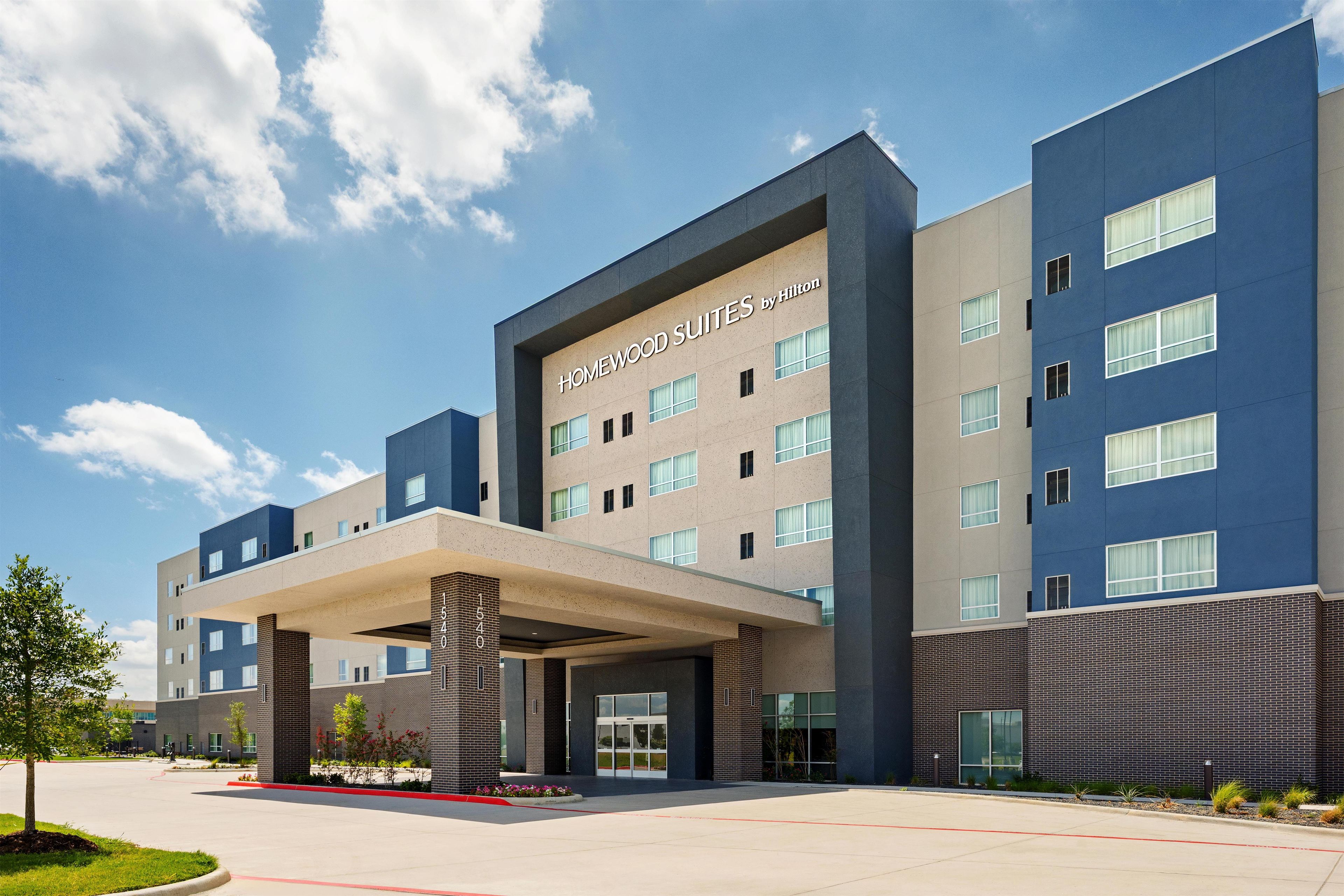 A modern hotel building with a prominent entrance, multiple floors, and a clear sky.