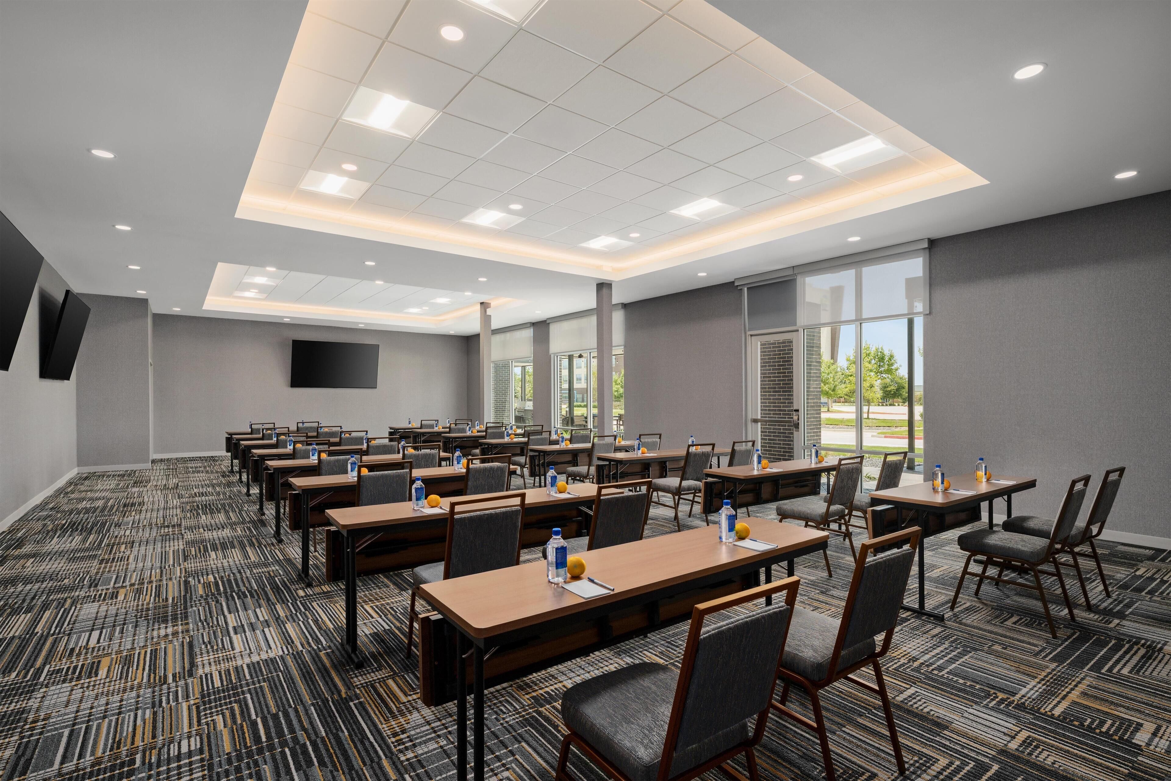 A conference room with multiple tables and chairs, large windows, and a flat-screen TV on the wall.