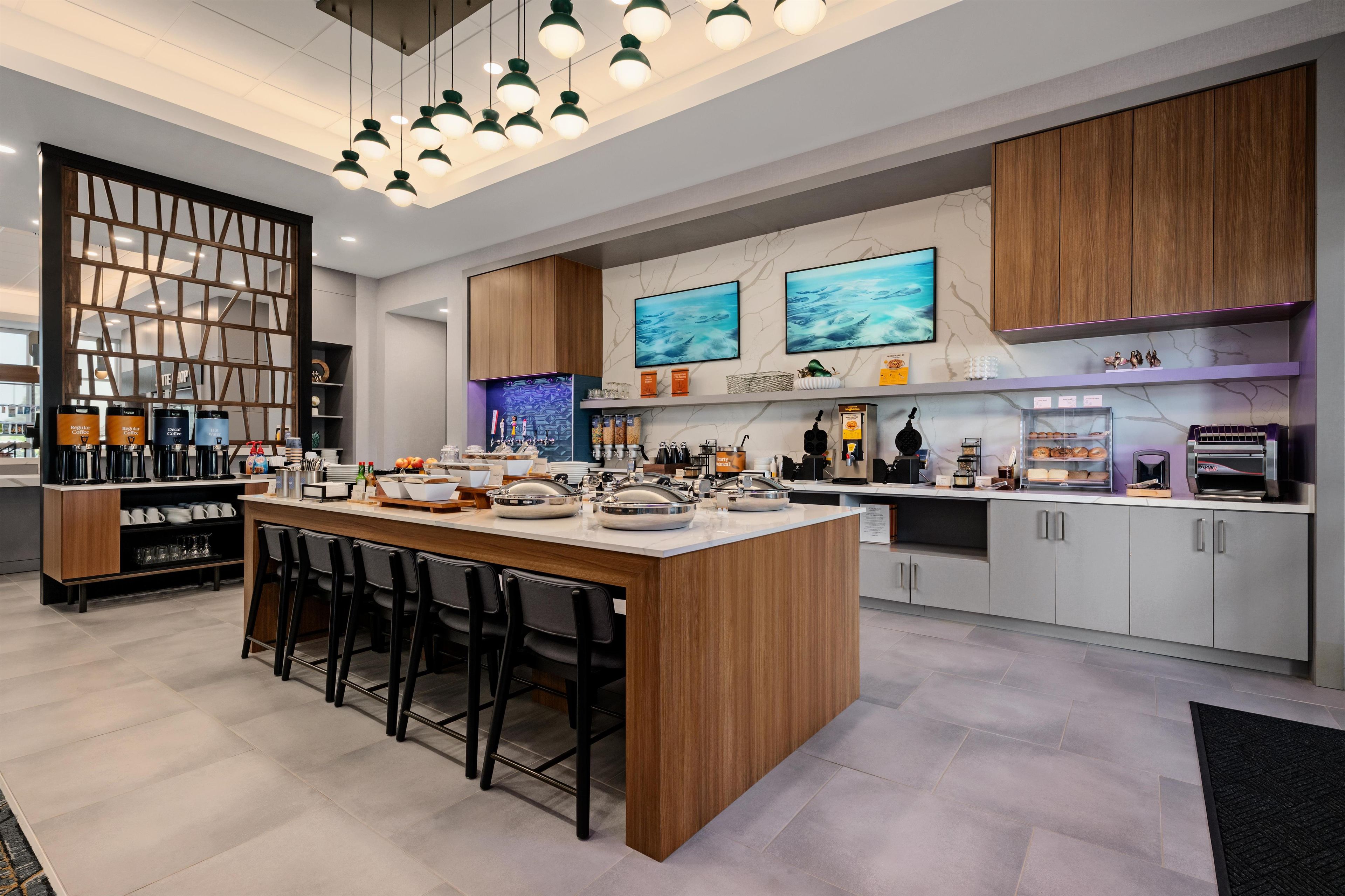A modern kitchen with a central island, bar stools, and a variety of appliances and storage cabinets.