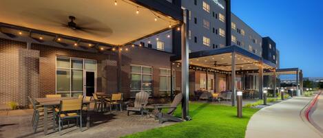 A hotel exterior with a covered outdoor seating area, a well-maintained lawn, and a clear sky.