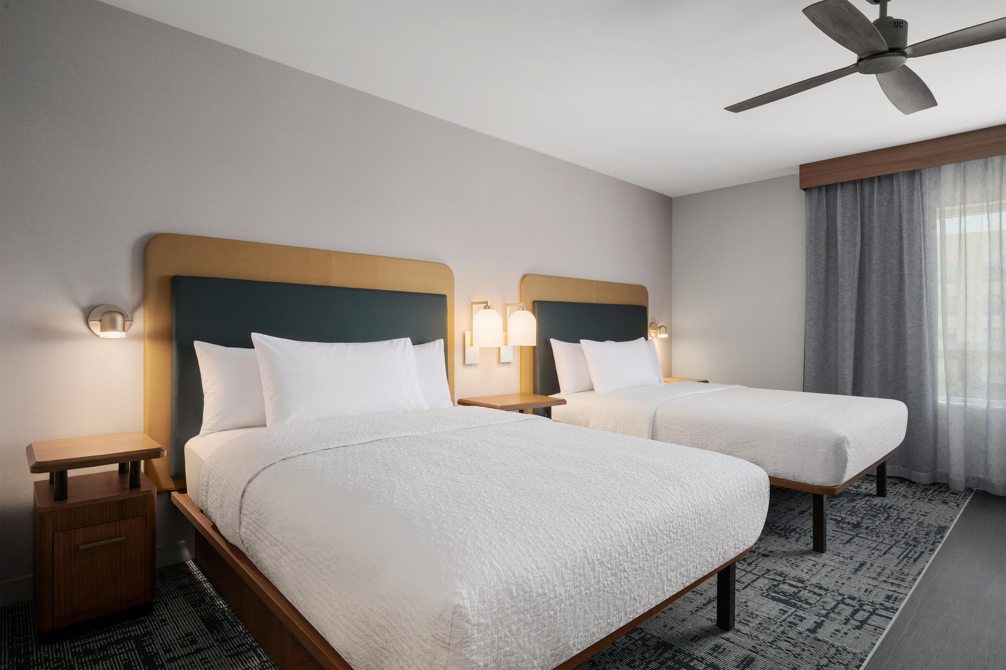 Une chambre d’hôtel avec deux lits, un ventilateur de plafond et une fenêtre avec des rideaux.