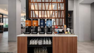 Una estación de café con cuatro dispensadores etiquetados como 'Café Regular', 'Café Descafeinado' y 'Agua Caliente', y una cafetera.