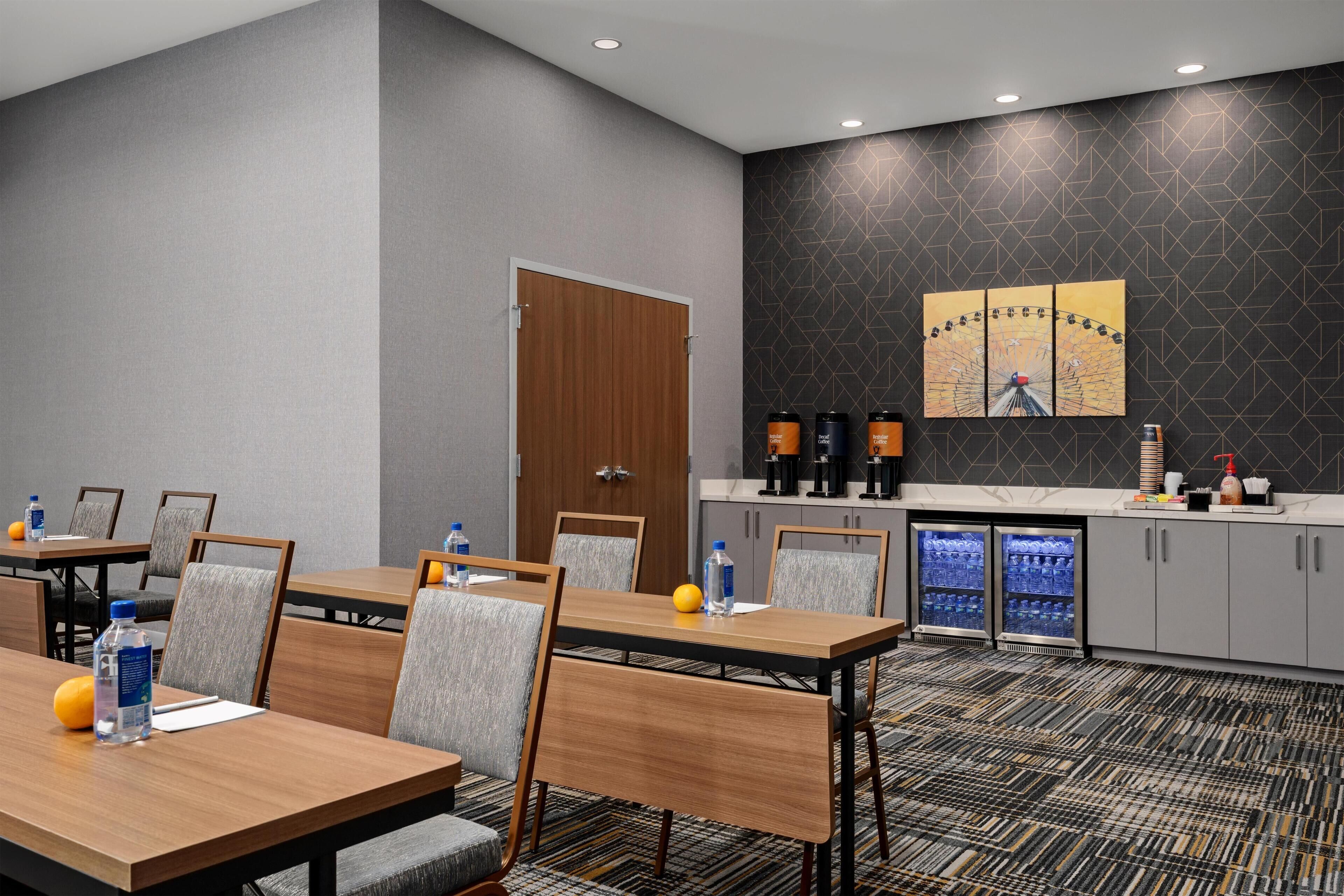 A hotel room with a conference table, chairs, a minibar, and a coffee station.