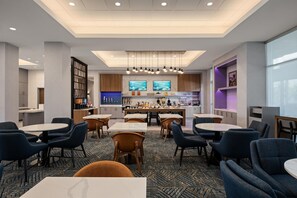 Un hall d’hôtel doté d’un bar central, de différents espaces aménagés pour s’asseoir et d’un tapis à motifs.