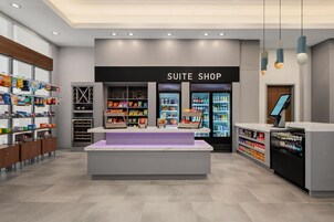 Una tienda de habitaciones de hotel modernas con un escaparate central, secciones refrigeradas y estanterías llenas de diversos productos.