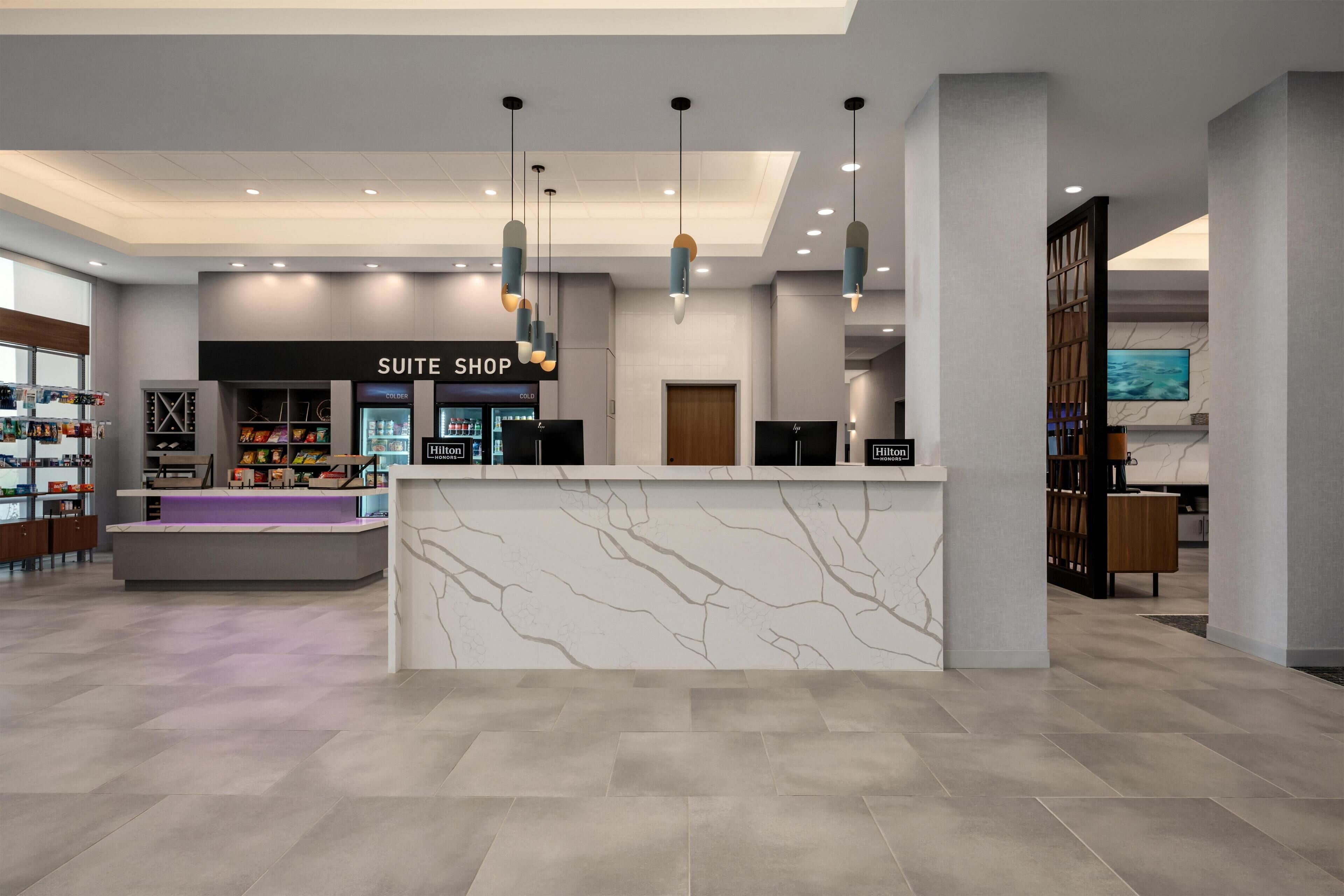 Um lobby de hotel moderno com uma receção, um letreiro 'Suite Shop' e um ecrã grande exibindo uma vista panorâmica.