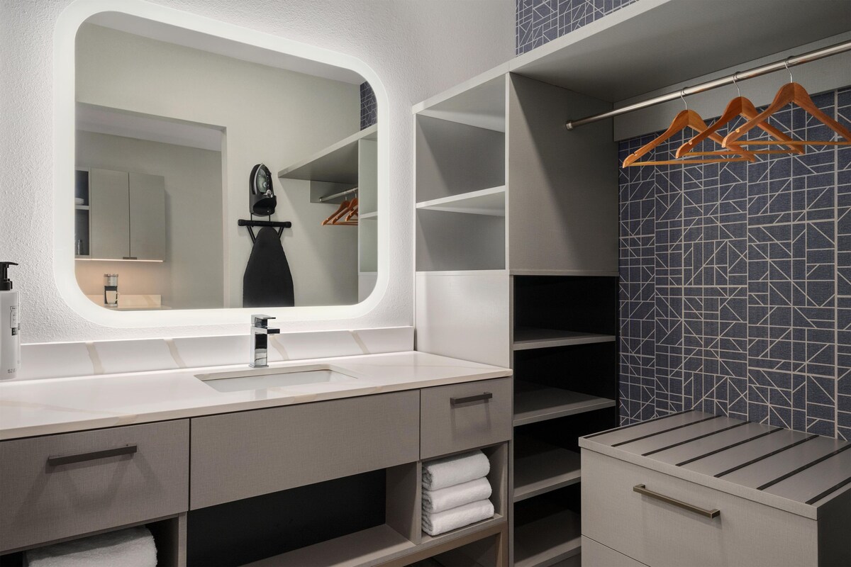Une salle de bain moderne avec un grand miroir, un lavabo et un placard intégré avec espace pour suspendre les vêtements.