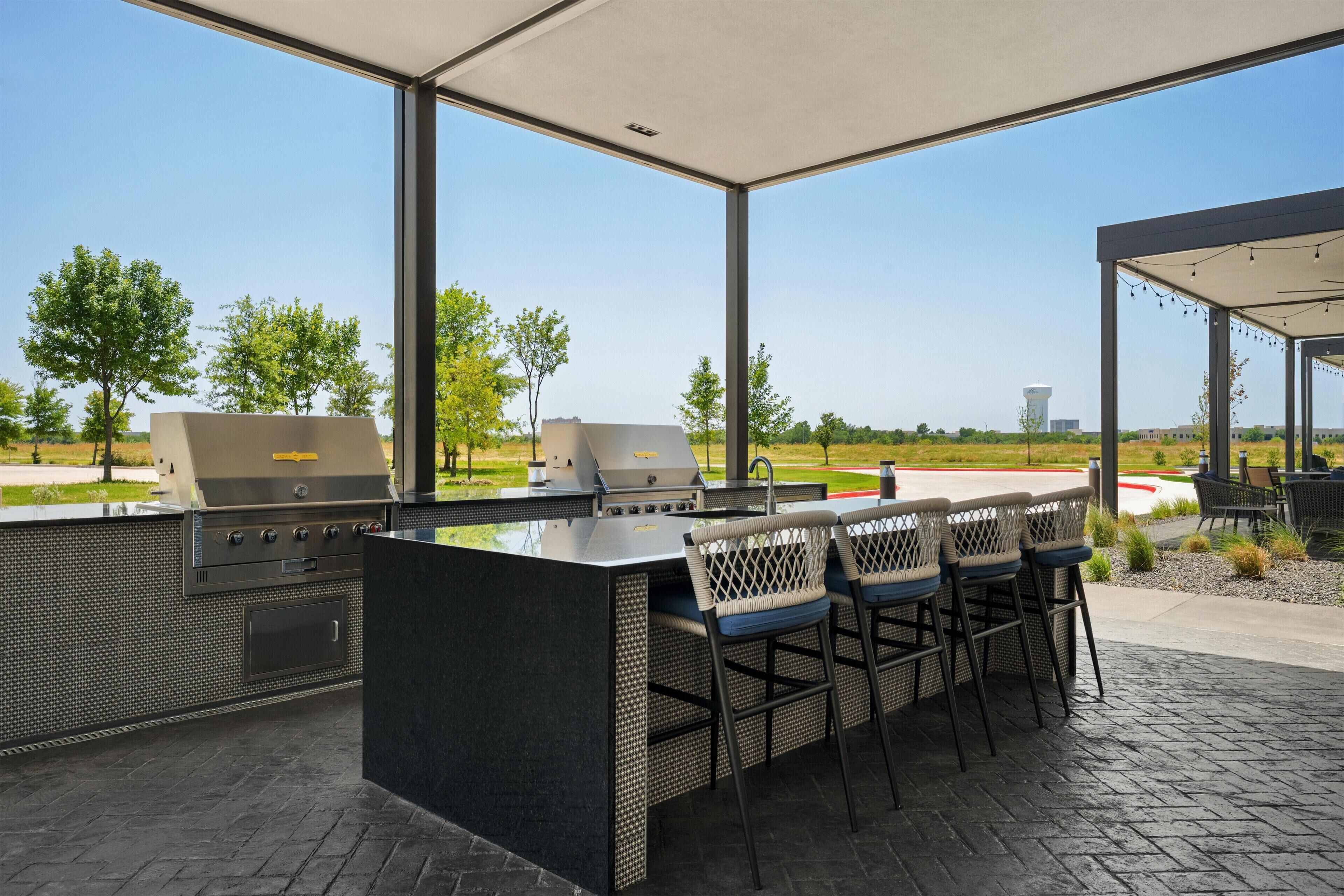 An outdoor barbecue area with a grill station, bar stools, and a view of a golf course.