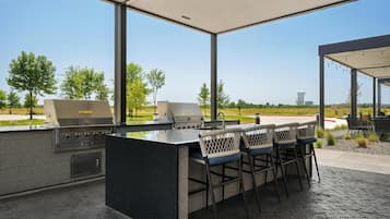 Ein Außenbereich mit Grillstation, Barhocker und Blick auf einen Golfplatz.