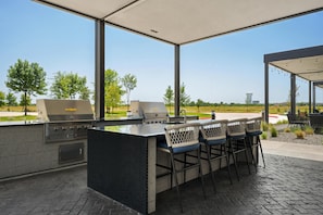 An outdoor barbecue area with a grill station, bar stools, and a view of a golf course.