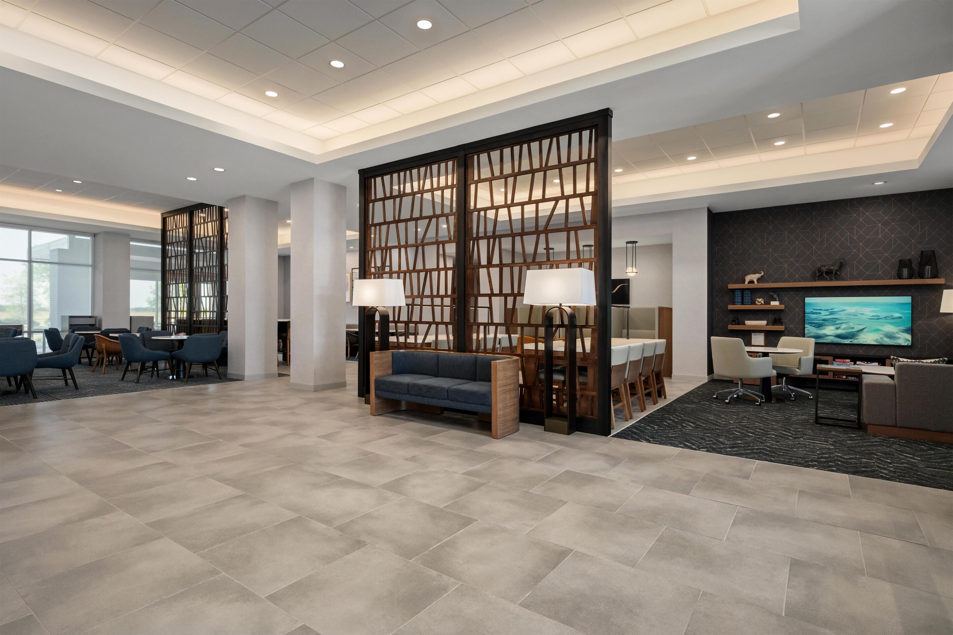 A modern hotel lobby with a seating area, a television, and a large window.