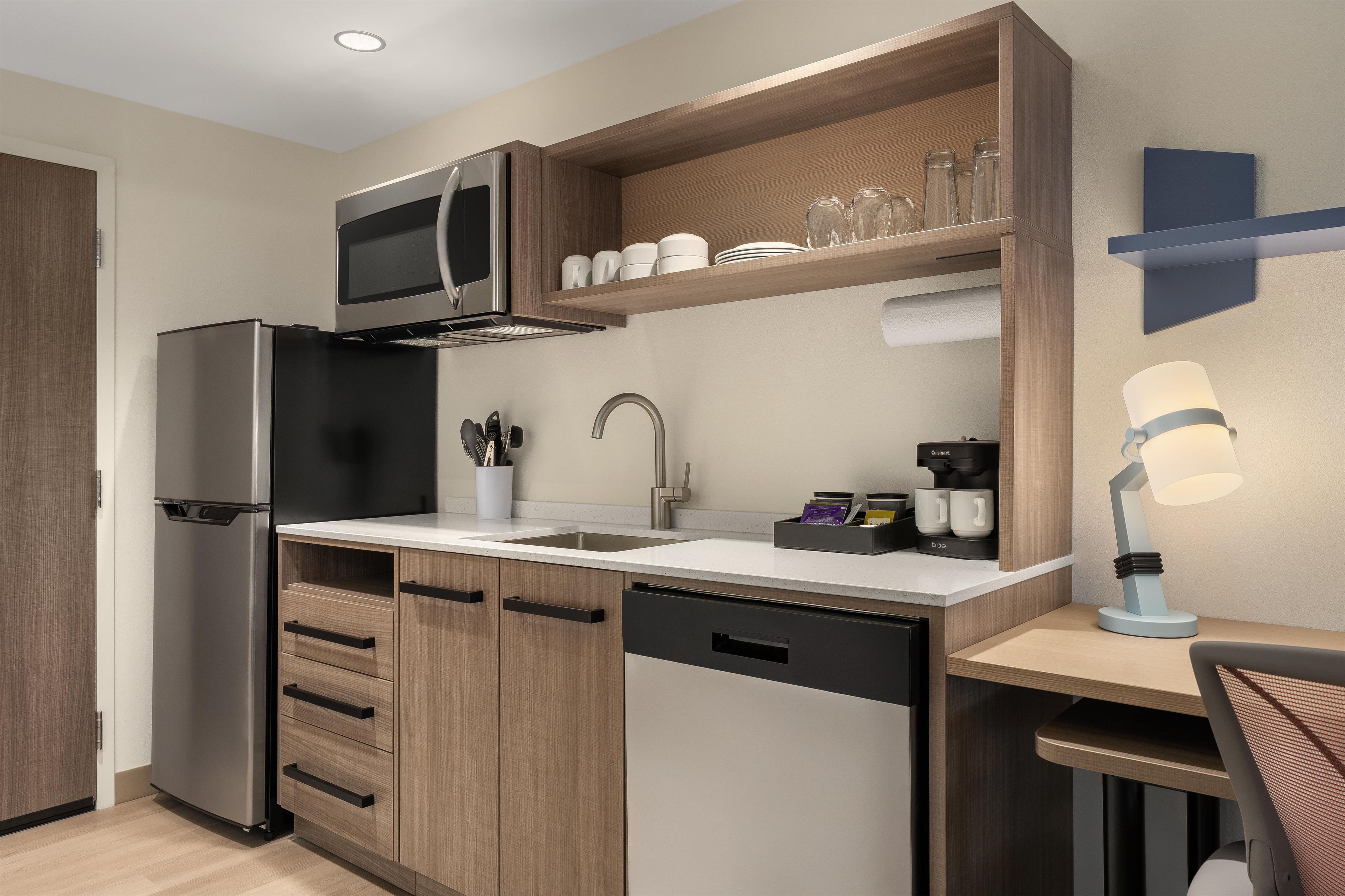 A compact kitchen with a built-in microwave, stainless steel refrigerator, wooden cabinets, a sink, and a coffee maker.