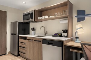 Cocina compacta con microondas integrado, refrigerador de acero inoxidable, gabinetes de madera, un lavamanos y cafetera.