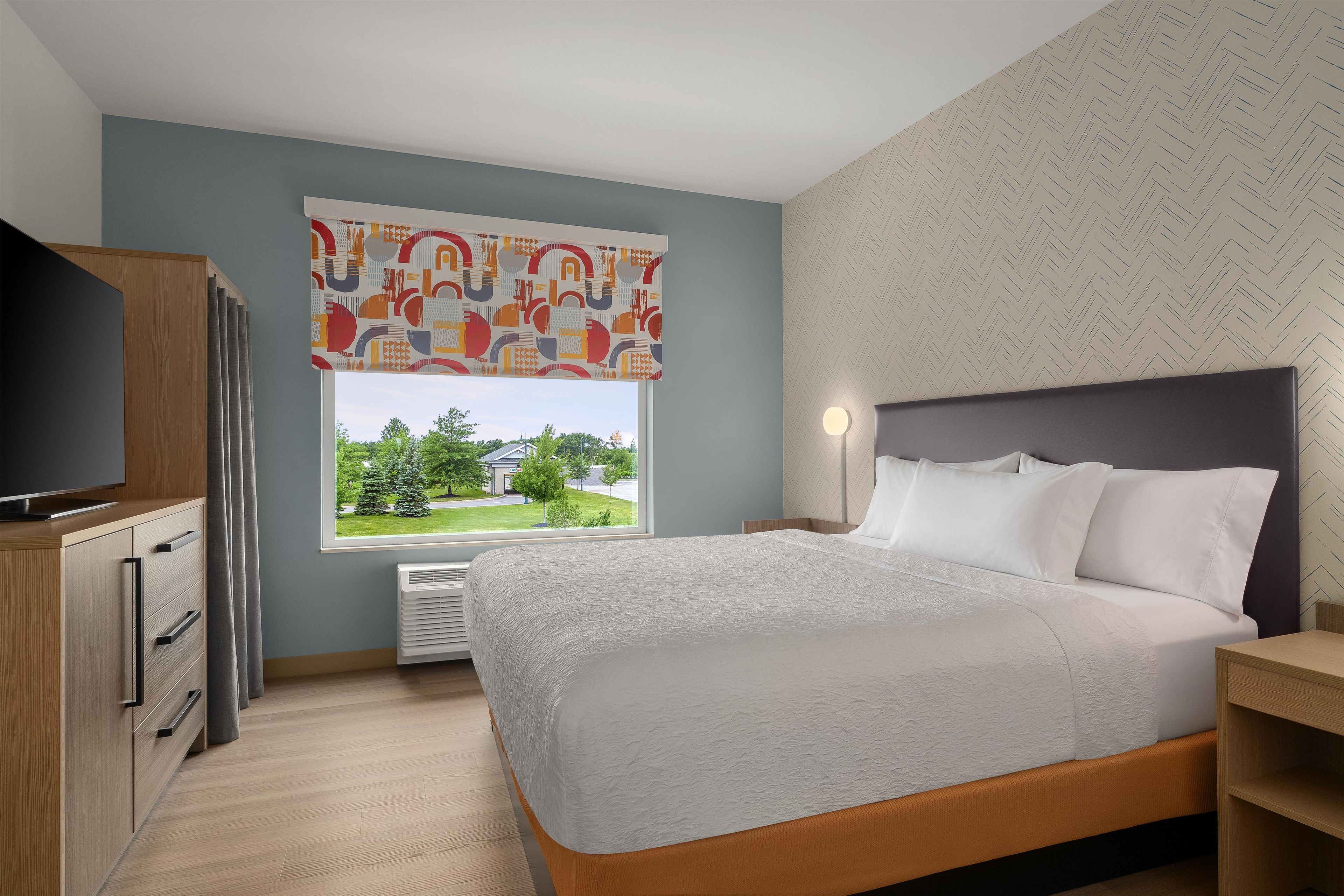 Een slaapkamer met een bed, een televisie, een raam met uitzicht en een behang met patroon.