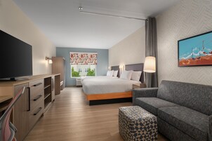 Una habitación de hotel moderna con cama, sofá, televisor y un cuadro en la pared.