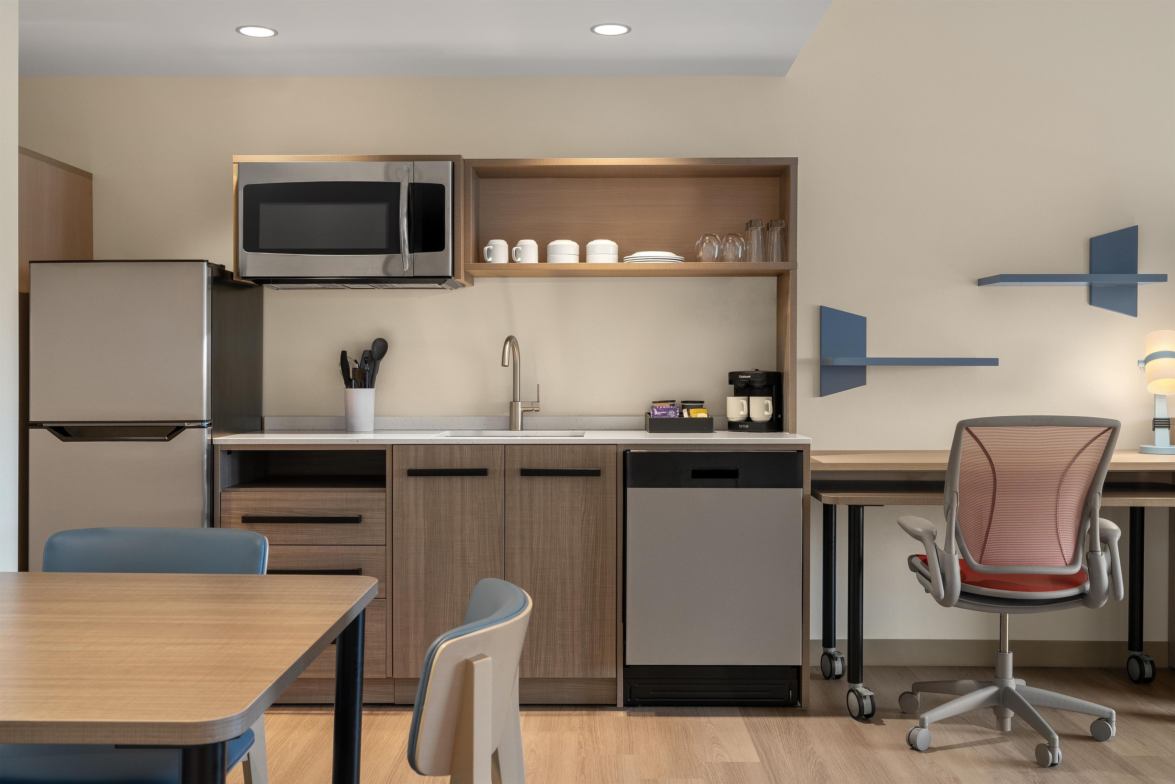 A modern kitchen with a built-in microwave, a sink, and a dishwasher. There is a dining table with chairs and a high chair with wheels.