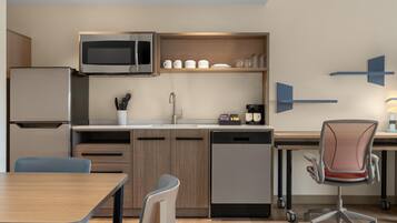 Una cocina moderna con microondas integrado, un fregadero y lavavajillas. Hay una mesa de comedor con sillas y una trona con ruedas.