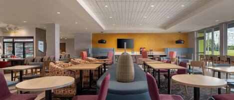 A modern dining area with multiple tables and chairs, a central seating area with a unique design, and a vending machine labeled 'SNACKS ARE'.