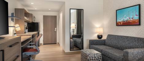 A modern hotel room with a desk, chair, sofa, ottoman, and a large mirror.