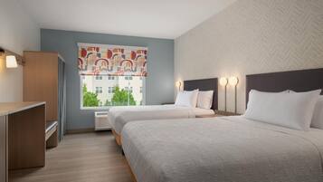 A hotel room with two beds, a desk, and a window with a view of buildings.