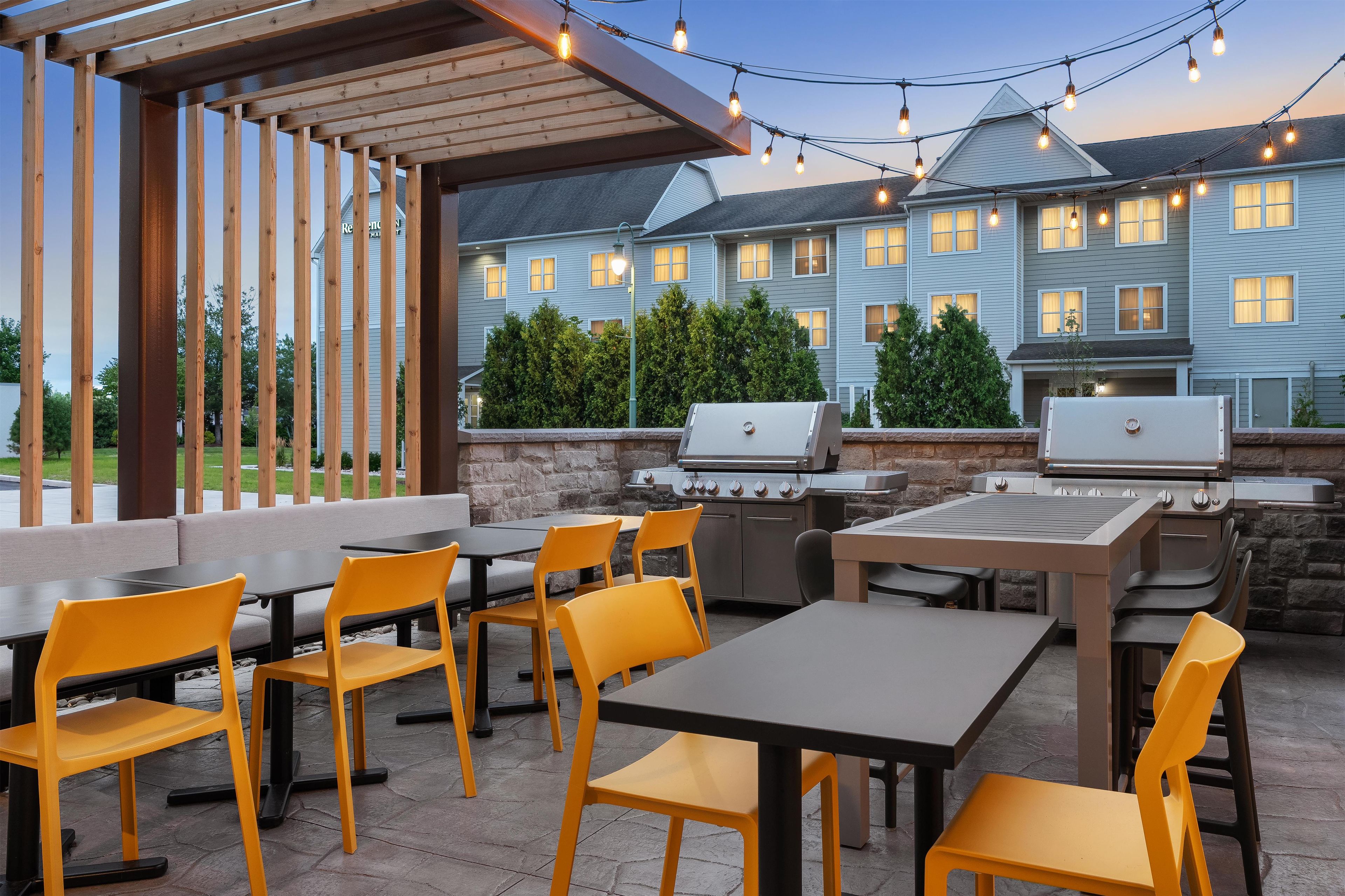 Un patio al aire libre con mesas, sillas, una parrilla y luces colgantes.