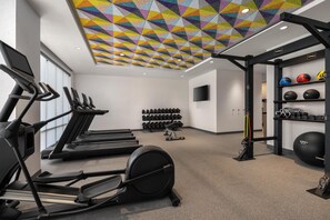 Un gimnasio con cintas de correr, máquinas de pesas y una variedad de mancuernas y pelotas de ejercicio.