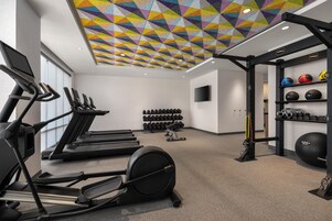 Un gimnasio con cintas de correr, máquinas de pesas y una variedad de mancuernas y pelotas de ejercicio.