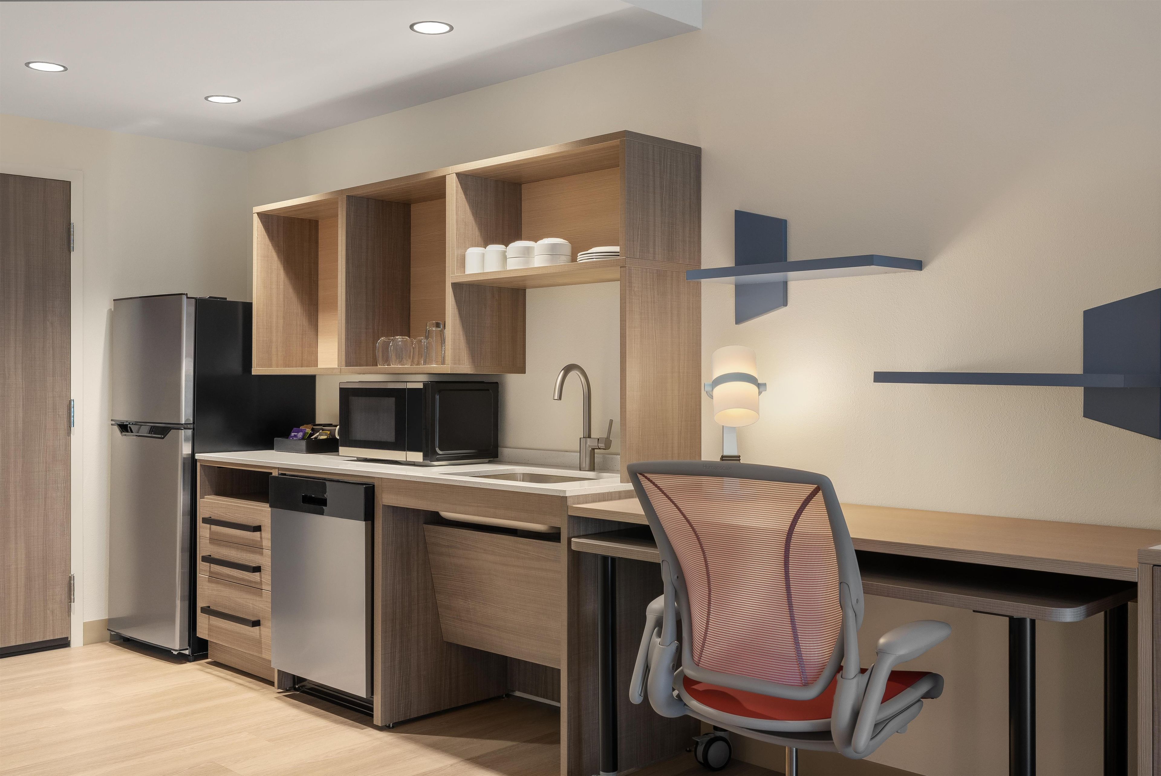 A modern kitchen with built-in appliances, a dining area with a chair, and a wall-mounted light fixture.