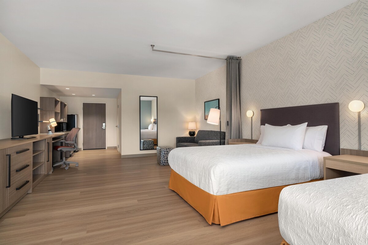 Une chambre d’hôtel comprenant un lit, des tables de chevet, un bureau avec une chaise, une télévision et une armoire.