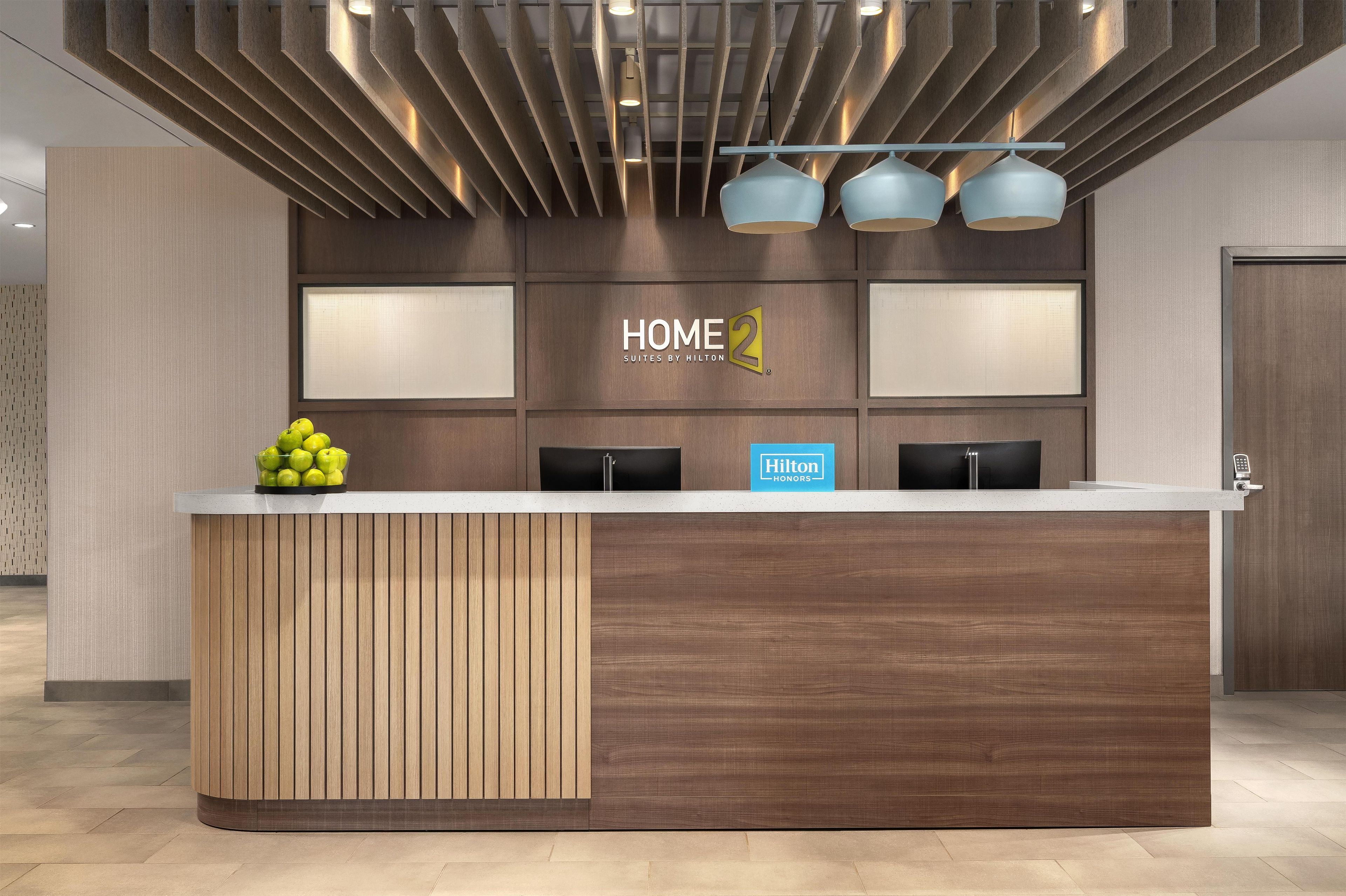 A hotel reception desk with a modern design, featuring a wooden panel and a glass display case with apples.