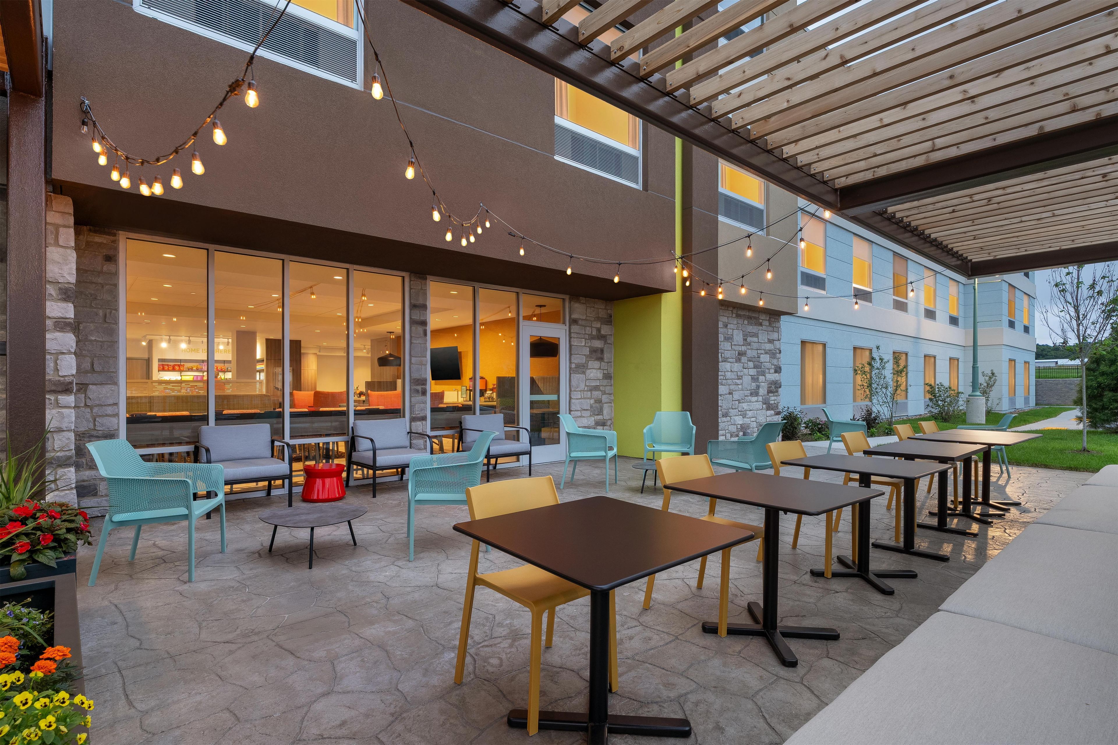 An outdoor patio with seating and tables, a stone wall, and a building with large windows in the background.