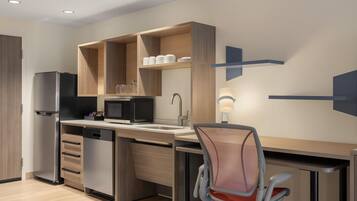A modern kitchen with built-in appliances, a dining area with a chair, and a wall-mounted light fixture.