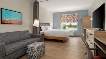 Une chambre d’hôtel avec un lit, un canapé, une télévision, un bureau et une fenêtre donnant sur un beau paysage.