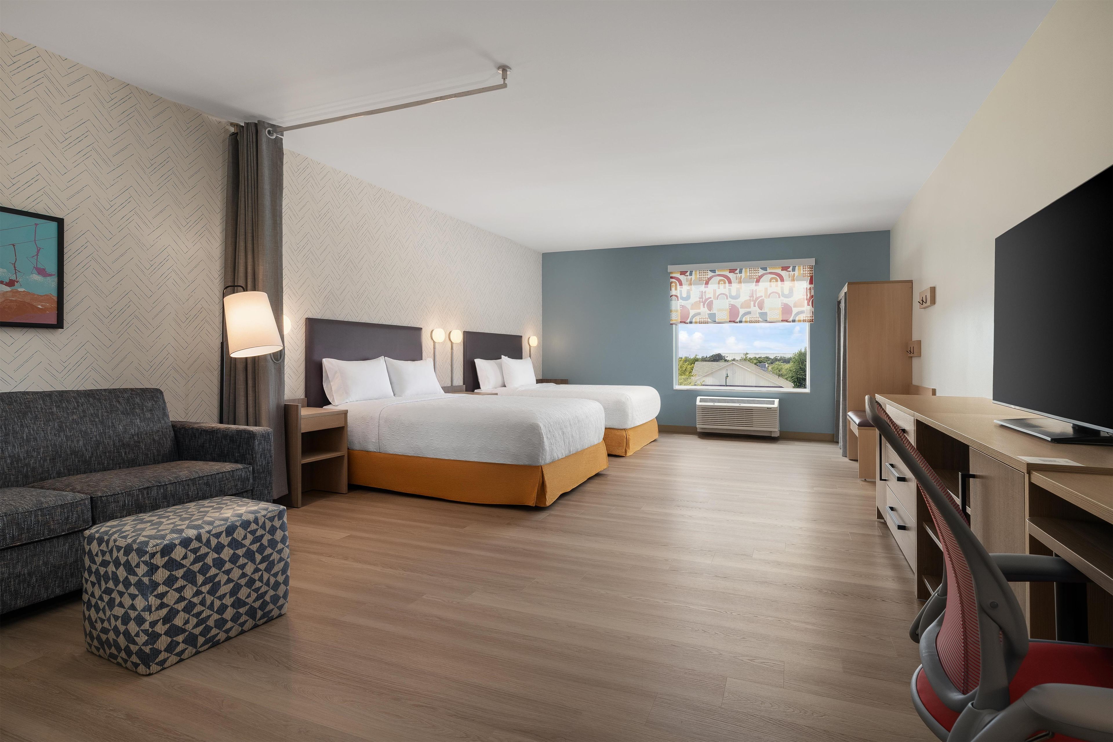 A modern hotel room with a bed, a desk, a chair, and a sofa.