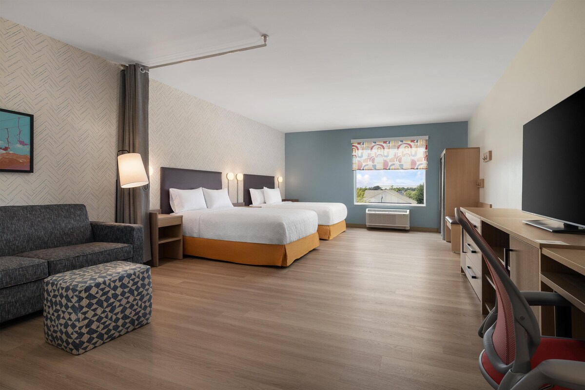 A modern hotel room with a bed, a desk, a chair, and a sofa.