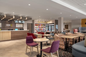 En modern hotellobby med en receptionsdisk, en sittgrupp och en bar där man kan köpa enklare mat och dryck.